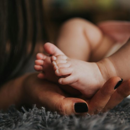Mano de una mujer junto a los pies de un bebé, imagen que representa la reflexión sobre tener hijos