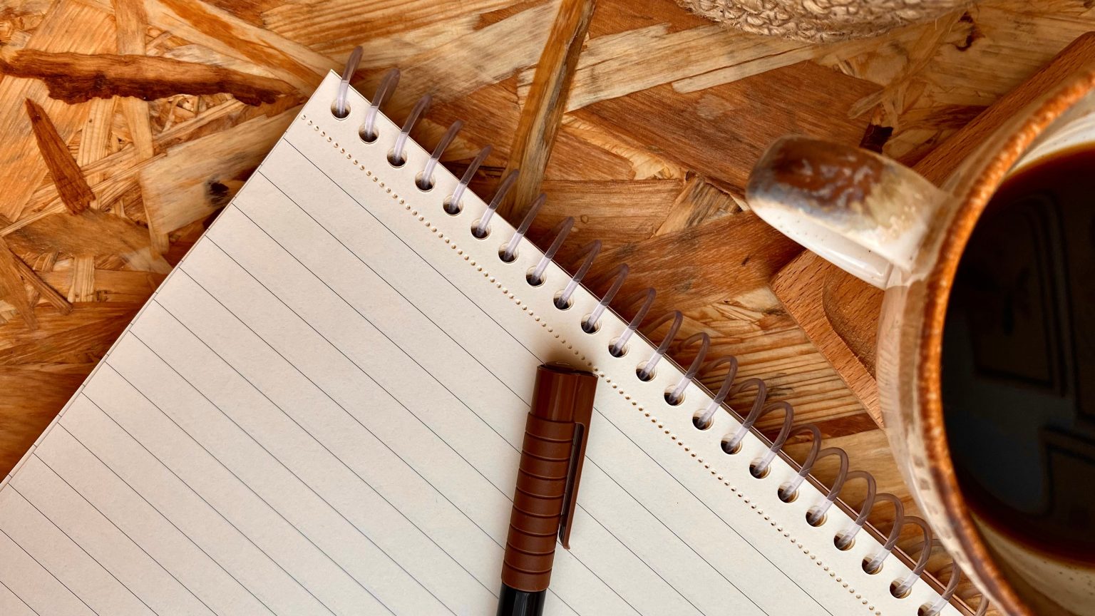 Libreta, bolígrafo y café en una mesa durante una sesión de estudio para oposiciones